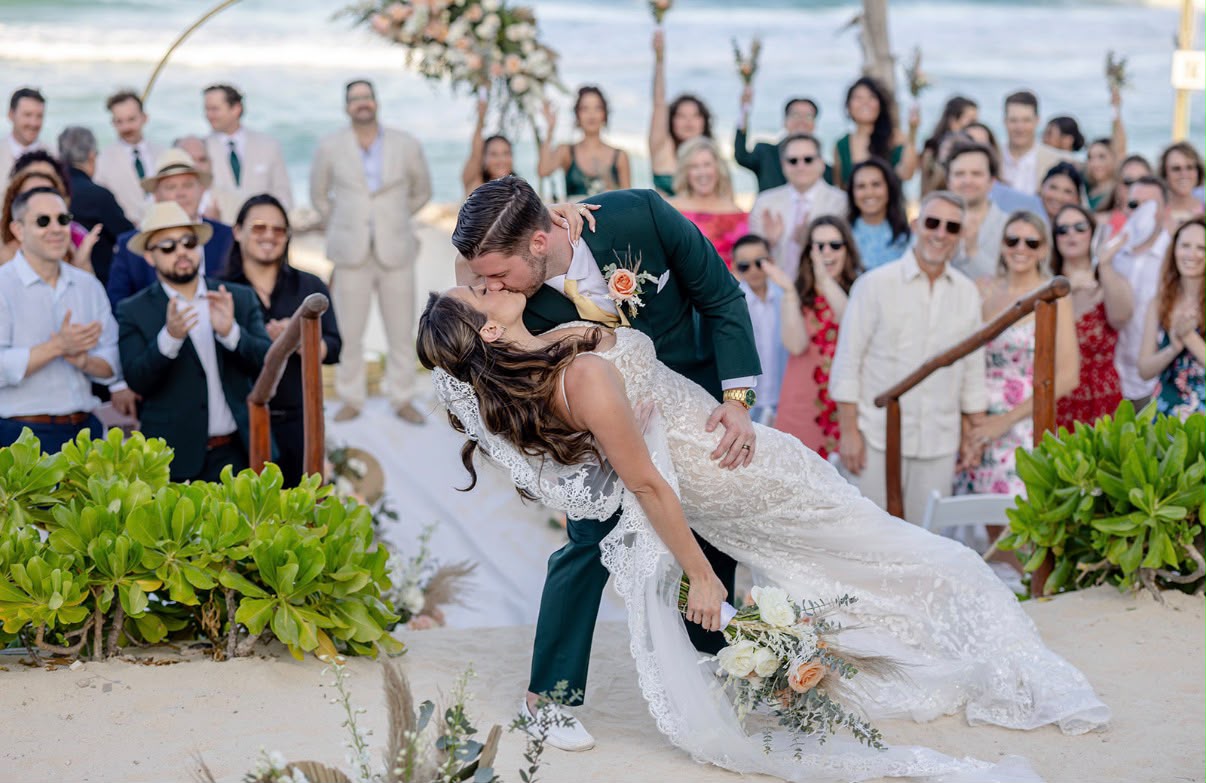 Beach ceremony dip kiss with guests celebrating